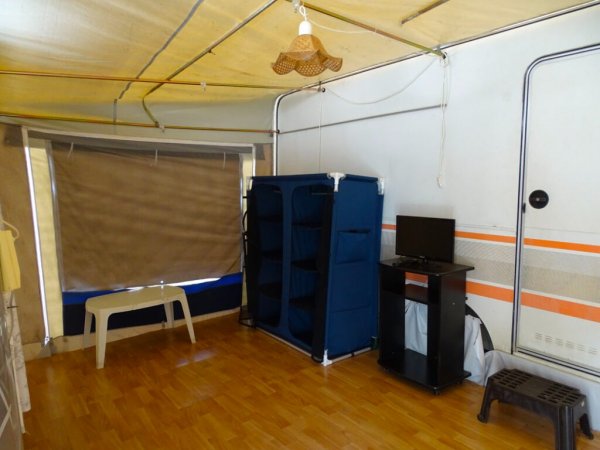 Interno di una tenda con mobile blu, piccolo televisore e pavimento in legno.