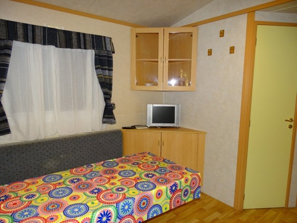 Stanza con letto colorato, TV su mobile e finestra con tenda scura.