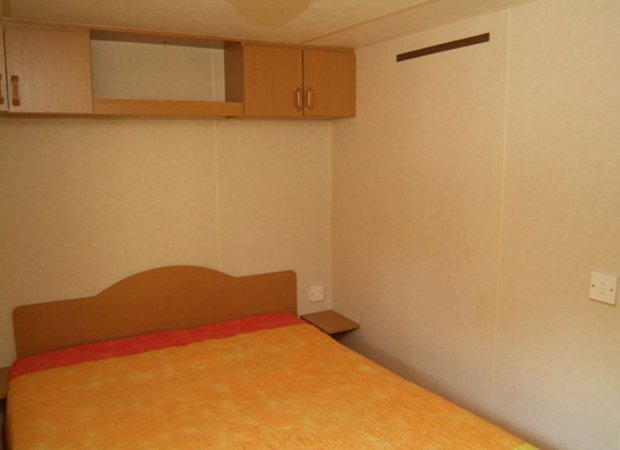 Camera con letto matrimoniale, copriletto arancione, armadio a muro.