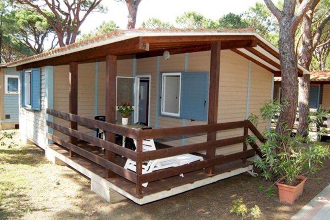 Bungalow in legno con veranda e vegetazione intorno.