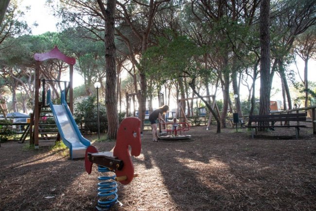 Un parco giochi con scivolo e giocattoli a molla, immerso in un'area boschiva.
