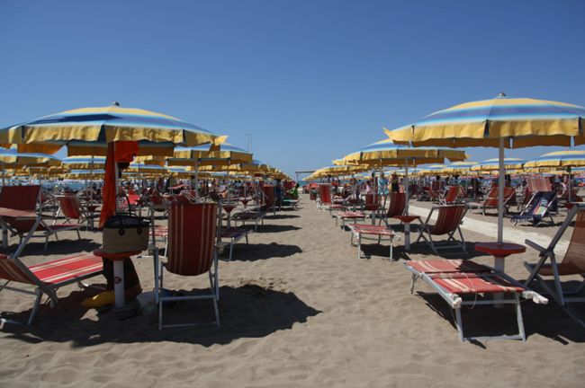 Ombrelloni gialli e blu con lettini a strisce rosse su una spiaggia sabbiosa.