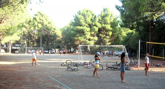 Ragazzi giocano a calcio in un campo all'aperto circondato da alberi.
