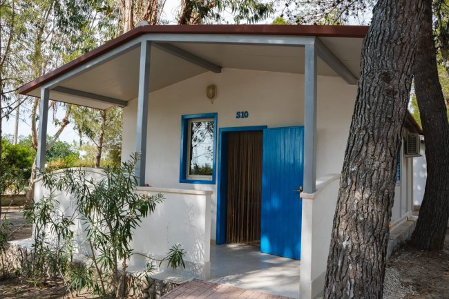 Bungalow bianco con porta blu in un bosco.