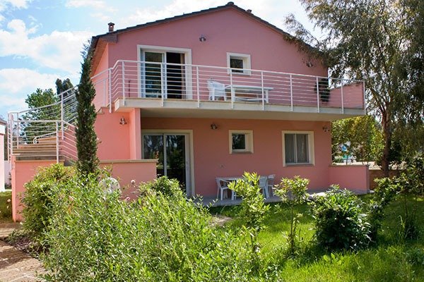 Casa rosa a due piani con balcone e giardino.