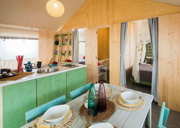 Cucina con dettagli in legno e verde, tavola apparecchiata e accesso a camera da letto.