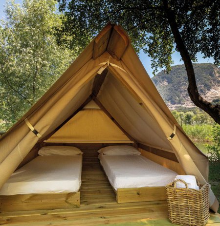 Tenda in legno con due letti singoli all'aperto, scenario naturale di sfondo.