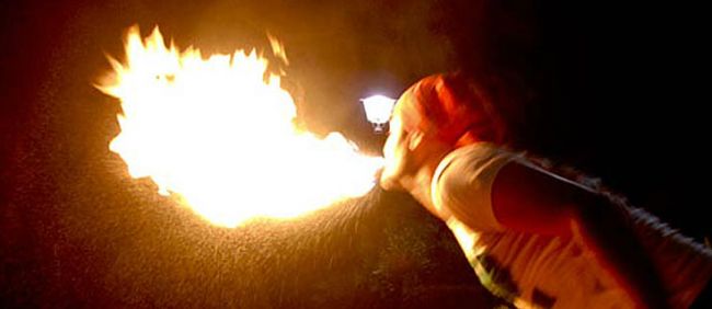 Persona che sputa fuoco in aria con sfondo scuro.