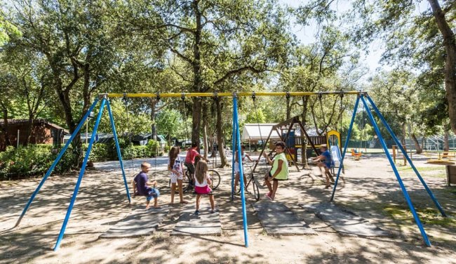 Bambini che giocano su altalene in un parco giochi immerso nella natura.