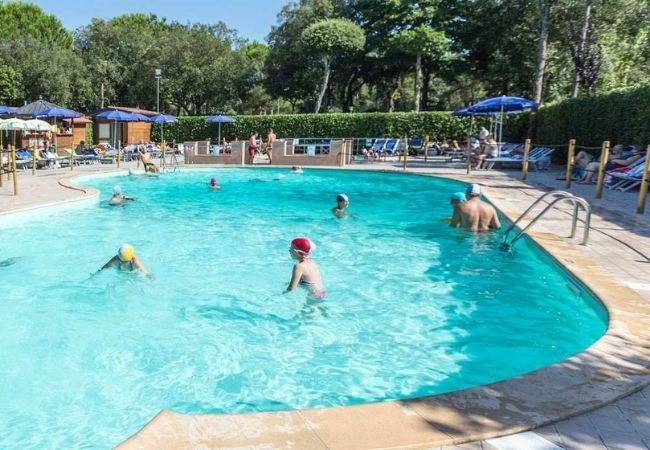 Persone che nuotano in una piscina all'aperto, con lettini e ombrelloni intorno.