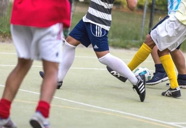 Persone che giocano a calcio su un campo all'aperto, concentrandosi sulle gambe e il pallone.