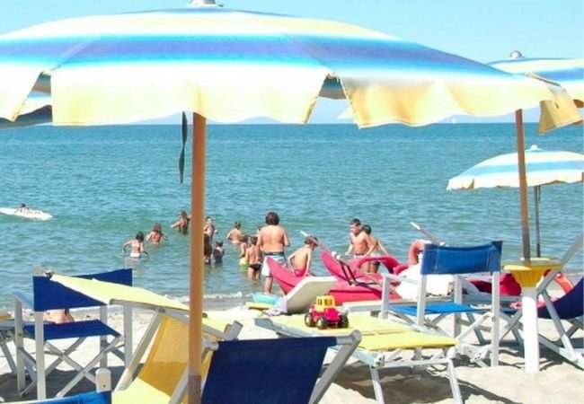 Spiaggia affollata, ombrelloni colorati, lettini e persone che si bagnano nel mare.