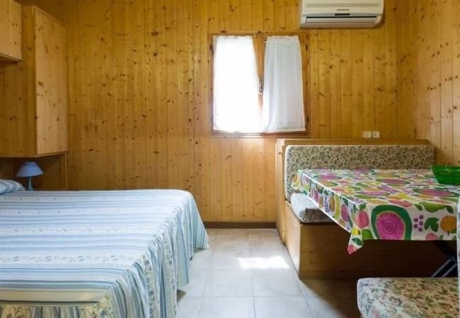 Stanza con pareti in legno, letto matrimoniale, tavolo con tovaglia colorata e aria condizionata.