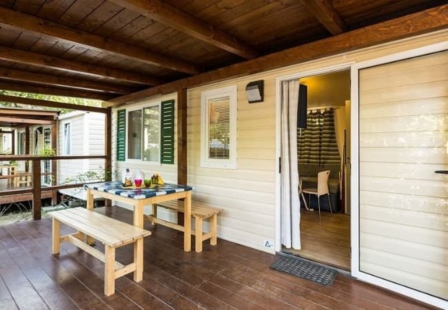 Una veranda in legno con tavolo e panche. Porta aperta che conduce all'interno della casa mobile.