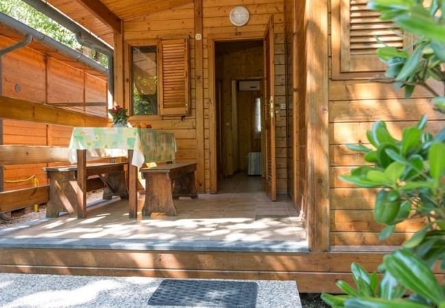 Veranda in legno con tavolo e panca, porta d'ingresso aperta.