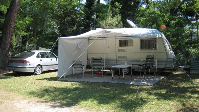 Camper con veranda e sedie vicino a un'auto.