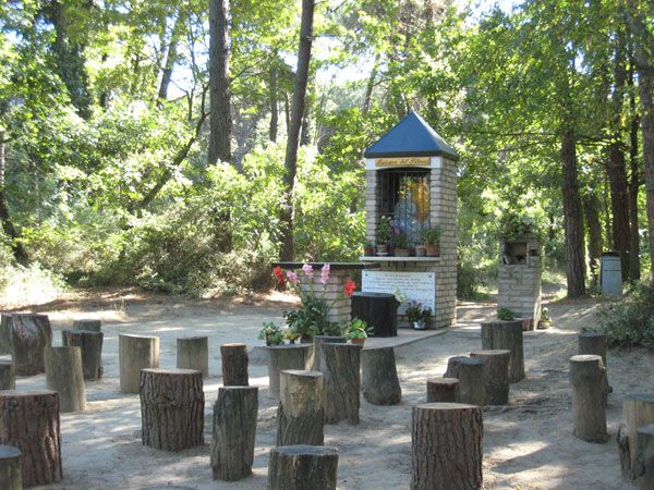 Un'edicola con statue, circondata da tronchi usati come sedili nel bosco.
