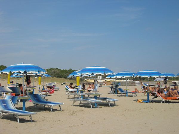Una spiaggia sabbiosa con ombrelloni blu e lettini, persone rilassate sotto il sole.