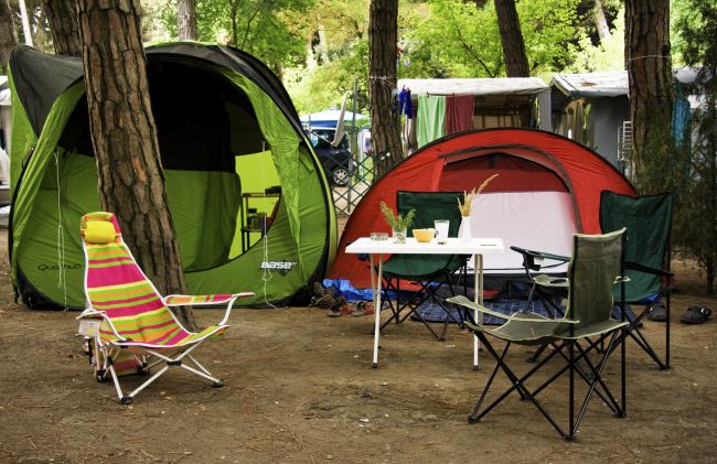 Due tende con sedie da campeggio e tavolo in un'area all'aperto tra gli alberi.