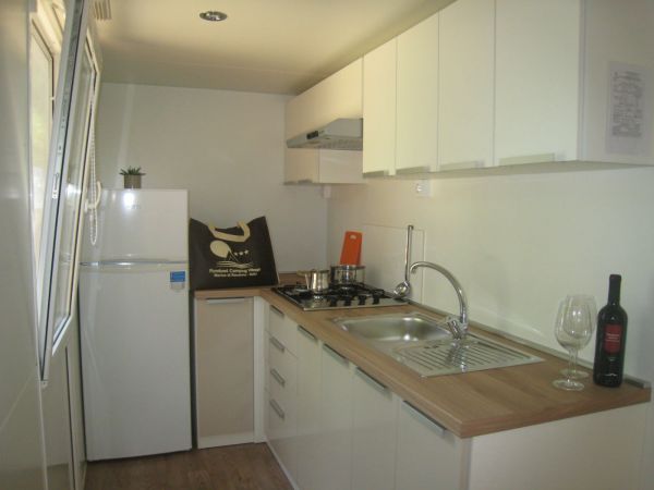 Cucina moderna con frigorifero, fornelli e lavabo, arredata con mobili bianchi.