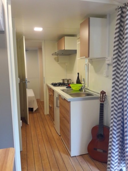 Cucina compatta con pavimento in legno e chitarra accanto al lavello.