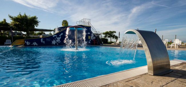 Piscina con fontane d'acqua e scivolo blu sullo sfondo.