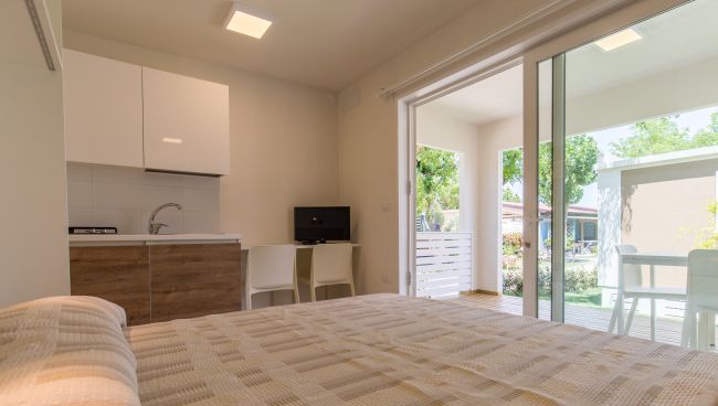 Interno monolocale con letto, angolo cottura e vista giardino.