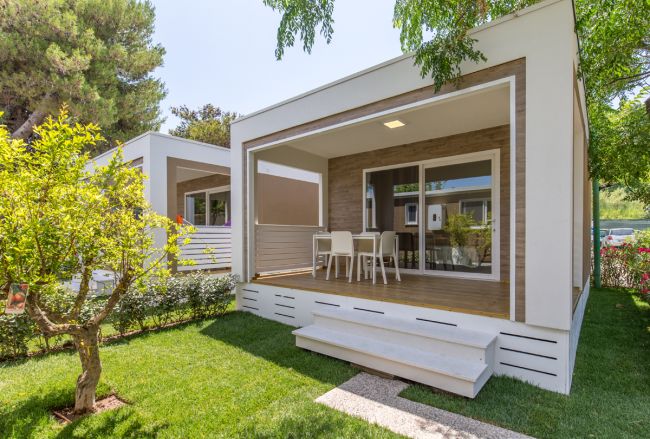 Modulo abitativo moderno con veranda, circondato da prato verde e piante.