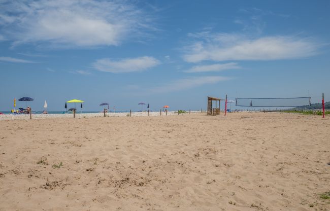 Una spiaggia di sabbia chiara con ombrelloni colorati e un campo da beach volley.