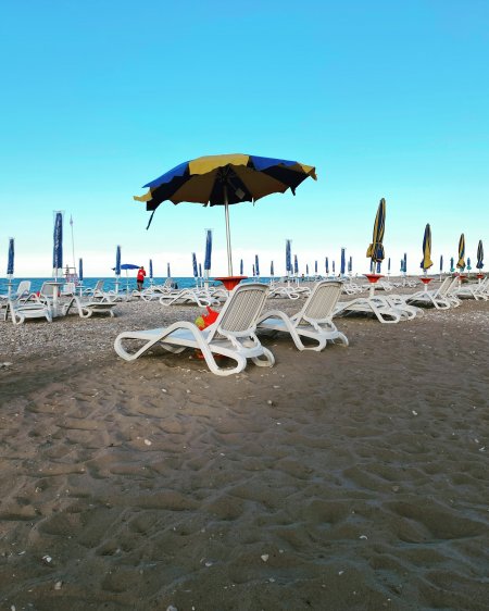 Sedie a sdraio e ombrelloni su una spiaggia sabbiosa sotto un cielo azzurro.