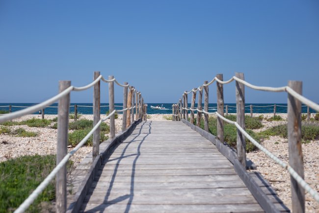 Passerella in legno con corde, che conduce verso il mare.