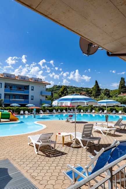 Una piscina con lettini e ombrelloni sotto un cielo blu, edificio sullo sfondo.