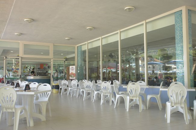 Esterno di un bar con tavoli e sedie bianche di plastica disposti ordinatamente.