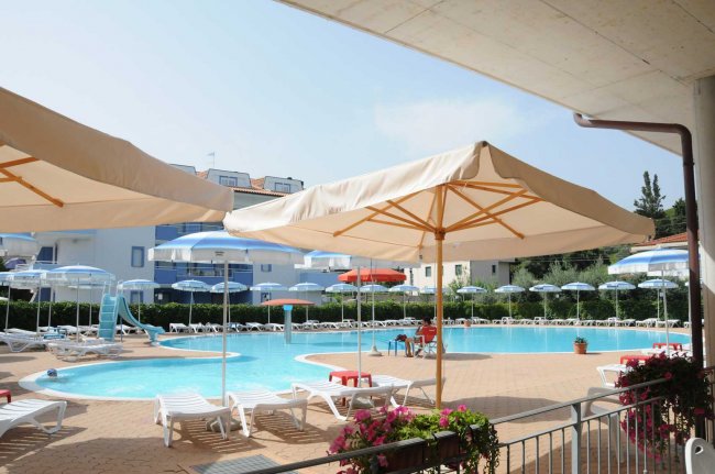 Grande piscina con ombrelloni di tela e sdraio bianche.