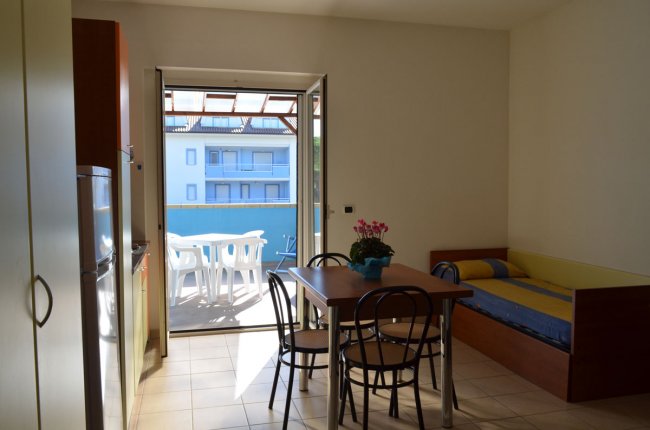 Stanza luminosa con tavolo, sedie, divano e porta finestra aperta.
