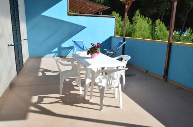 Terrazza con tavolo bianco, sedie e piante in vaso.