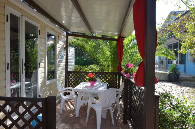 Veranda con tavolo bianco e sedie, circondata da piante e tendine rosse.