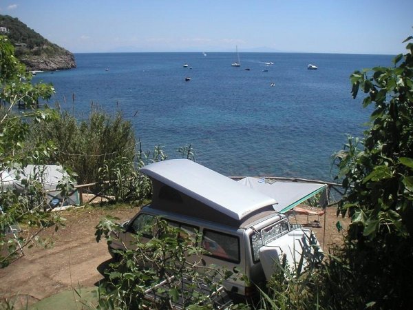 Un camper vicino al mare con vista su barche e scogli.