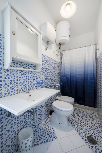Bagno con motivi blu, doccia con tenda sfumata e specchio sopra il lavandino.