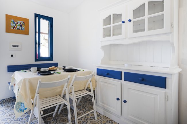Sala da pranzo con tavolo apparecchiato, credenza bianca e blu, pavimento decorato e finestra.