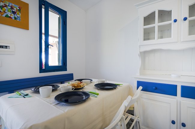 Sala da pranzo con tavolo apparecchiato, credenza bianca e blu, e finestra con cornice blu.