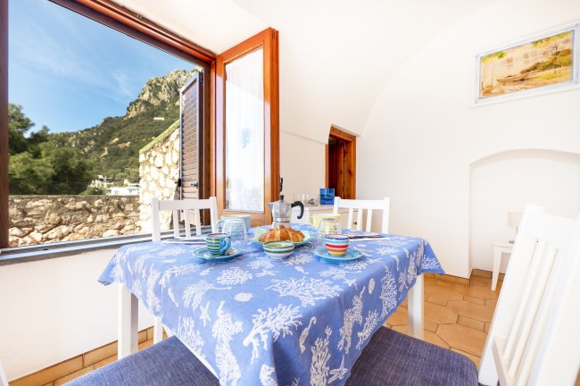 Tavolo apparecchiato con tovaglia blu e vista su paesaggio montuoso attraverso la finestra.