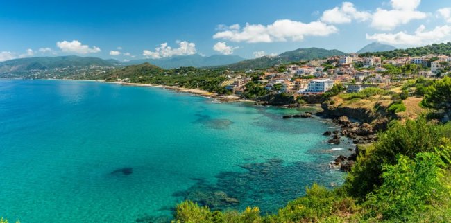 Costa panoramica con acqua turchese e case.