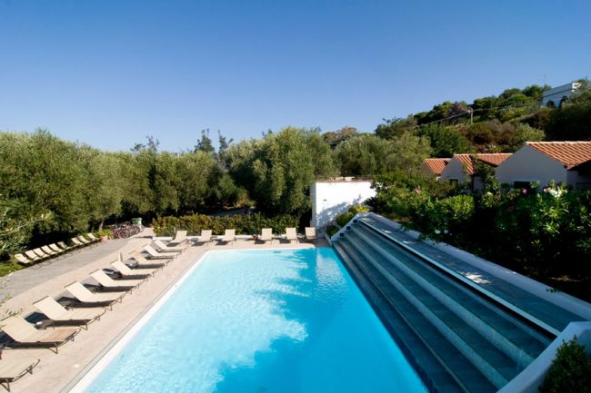 Piscina con sdraio disposte lungo i lati e vegetazione circostante.