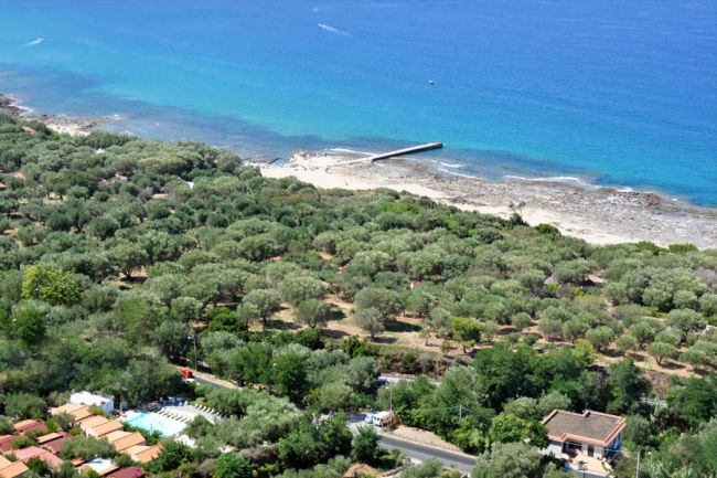 Veduta dall'alto di una costa, mare blu, vegetazione e bungalow.