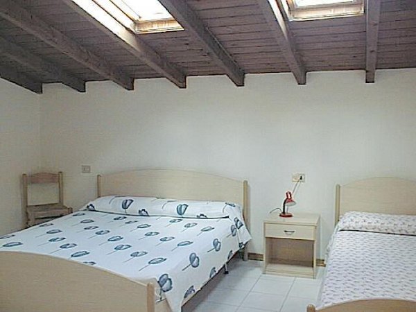 Stanza con letto matrimoniale e singolo sotto un soffitto di legno.