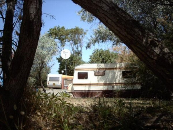 Roulotte parcheggiata tra alberi, visibile una parabola satellitare.