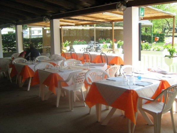 Terrazza esterna di un ristorante con tavoli apparecchiati e tovaglie arancioni.