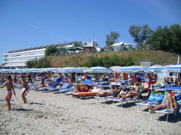 Spiaggia affollata con ombrelloni blu e persone sdraiate su lettini.