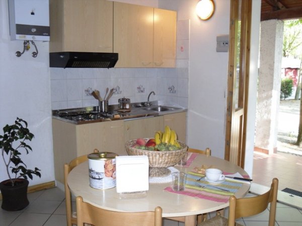 Cucina con tavolo rotondo e frutta, scaffali chiari e piante.